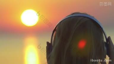 一个金发女人戴着无线耳机的<strong>特写</strong>背影，金色的日落在海上作为背景
